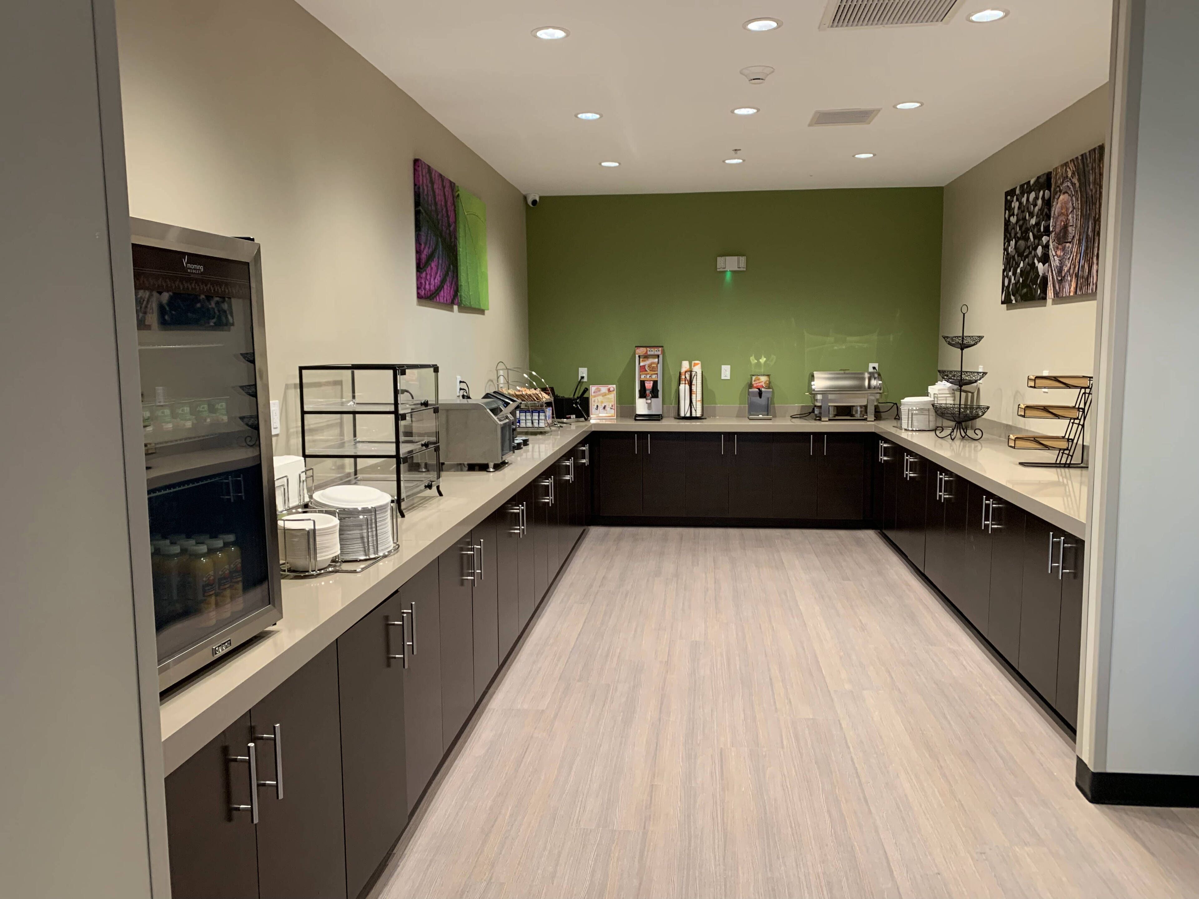 A modern kitchen with dark cabinets, a light countertop, and a green accent wall.