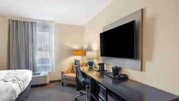 A hotel room with a bed, a desk, a chair, a television, a lamp, and a window with curtains.