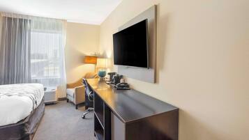 Habitación de hotel con cama, escritorio, silla, lámpara y televisor de pantalla plana montado en la pared.