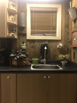 Compact kitchen with sink, window, and wooden cabinets, featuring a potted plant and decorative items.