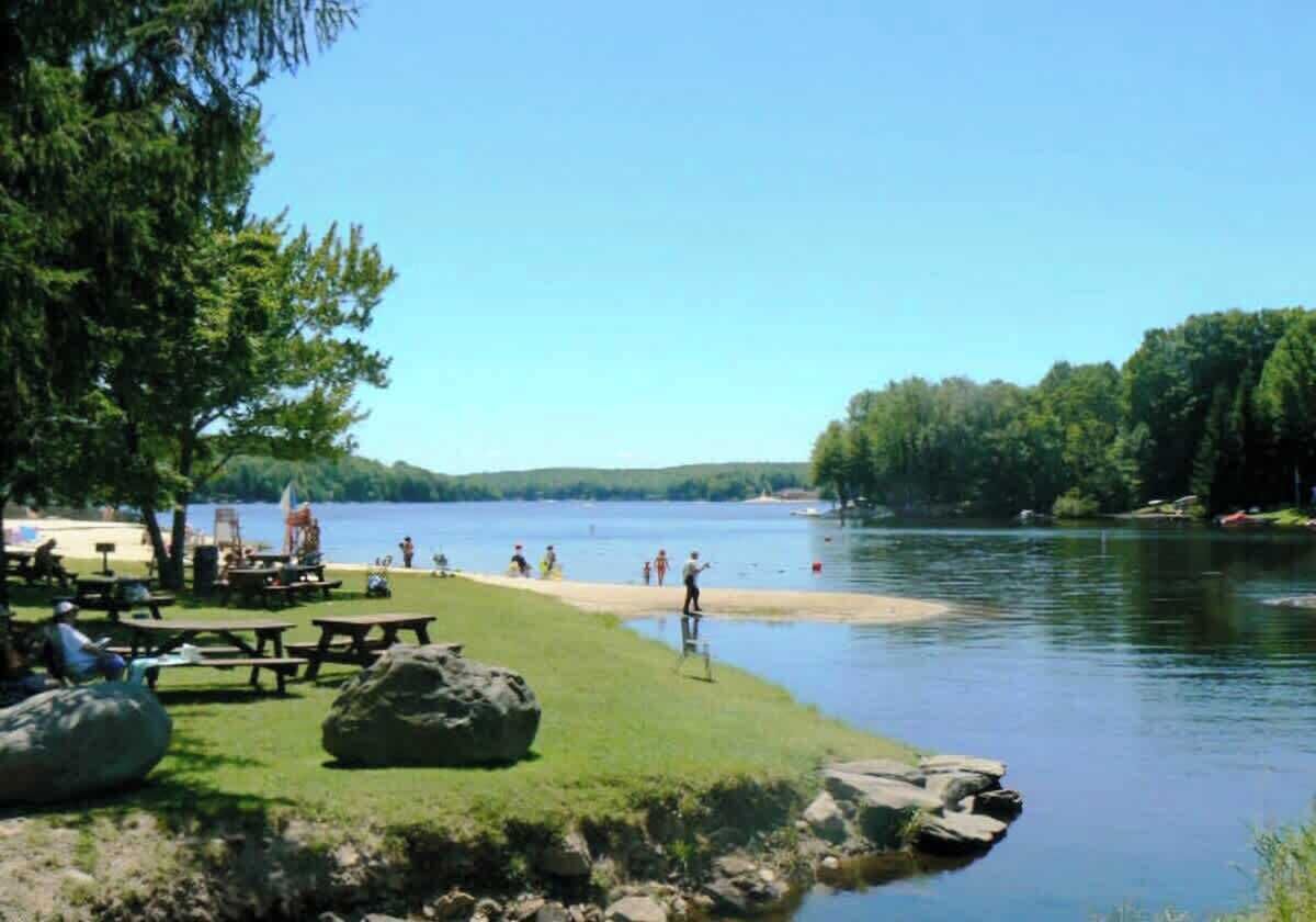 A lakeside picnic area with tables and benches, surrounded by trees and a calm lake.