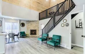 Amplia sala de estar con chimenea, una escalera y un comedor con sillas.