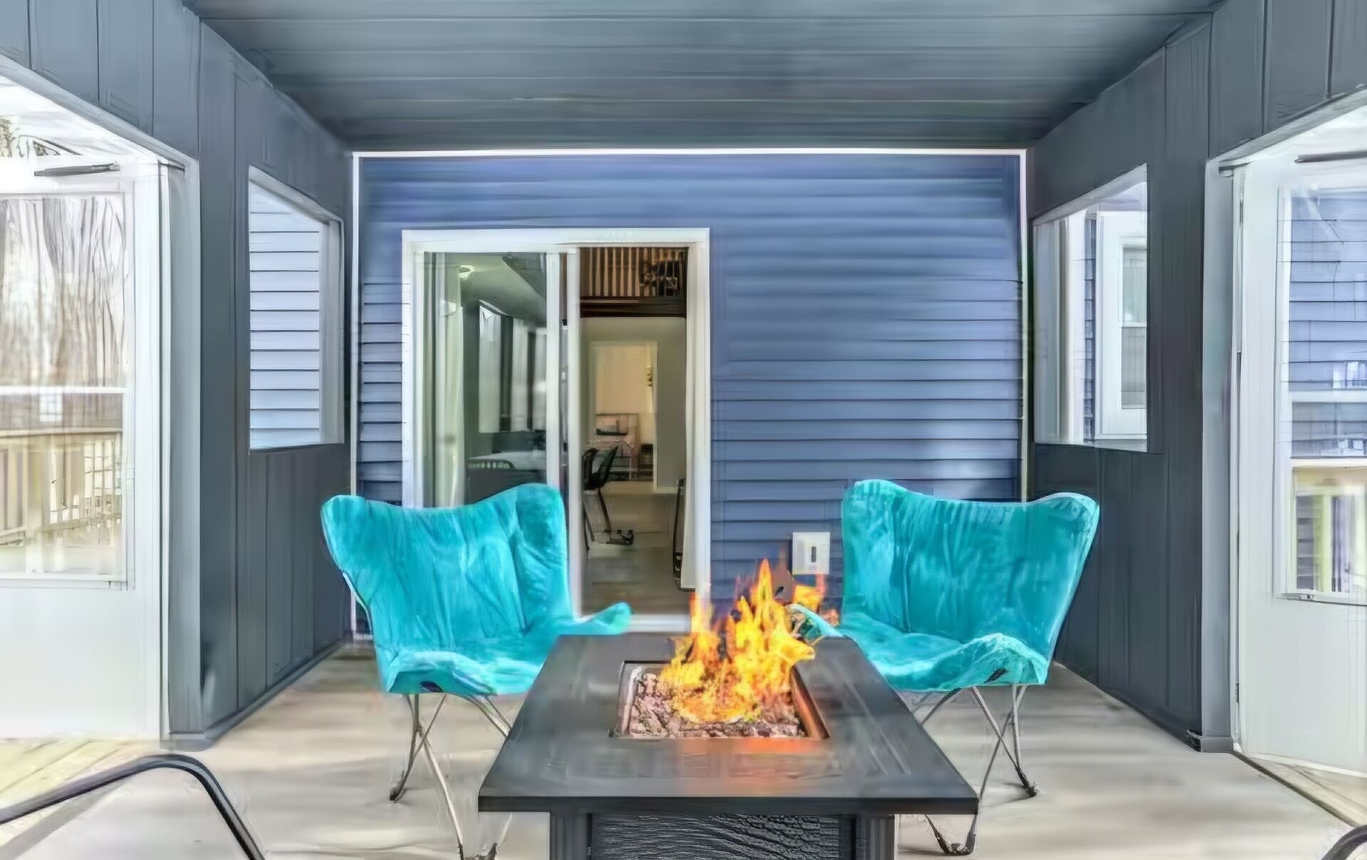 Un patio couvert avec un foyer, deux chaises et une vue sur l’intérieur de la maison.