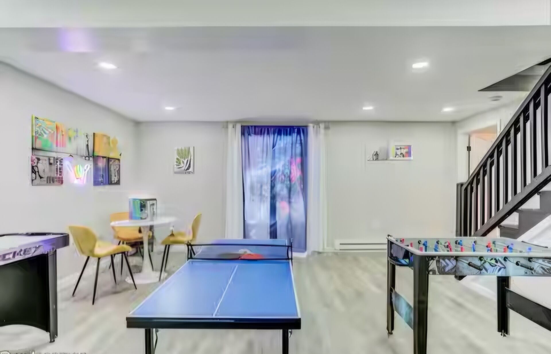 Une pièce comprenant une table de ping-pong, un bureau, des chaises, un escalier et des œuvres d’art accrochées aux murs.