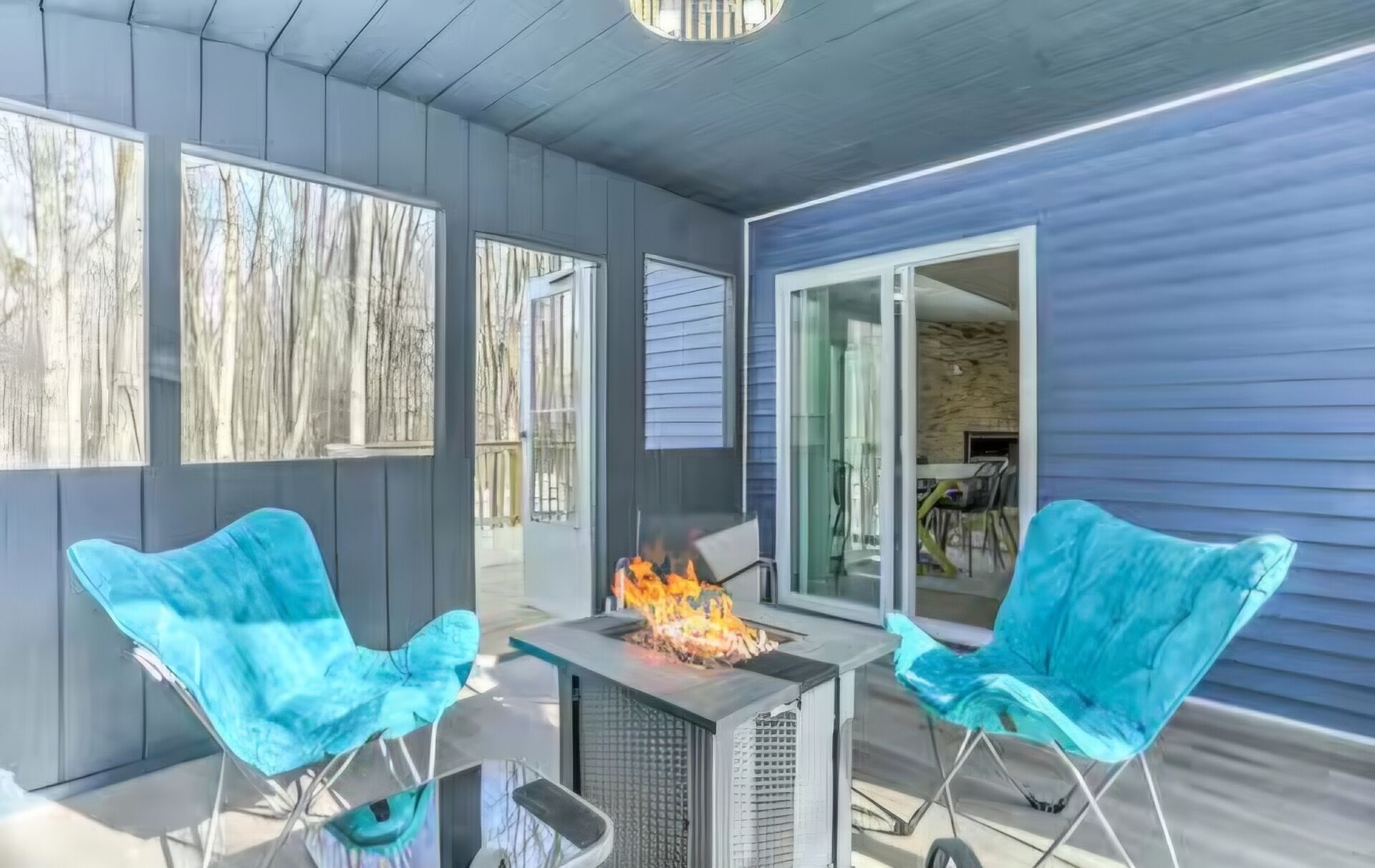 An outdoor patio with a fire feature, two chairs, and a view of the interior.