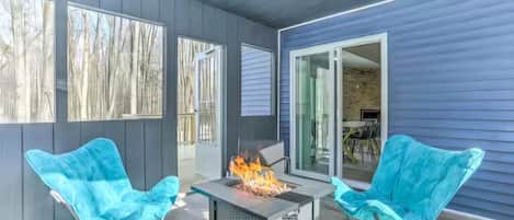 Une terrasse extérieure avec un foyer, deux chaises et une vue sur l’intérieur.