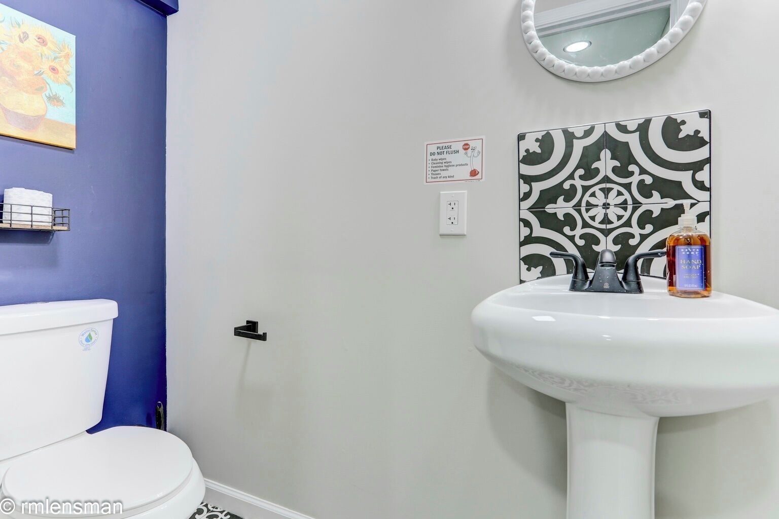 Un baño con un lavamanos blanco, un espejo, una botella de jabón para manos y un inodoro.