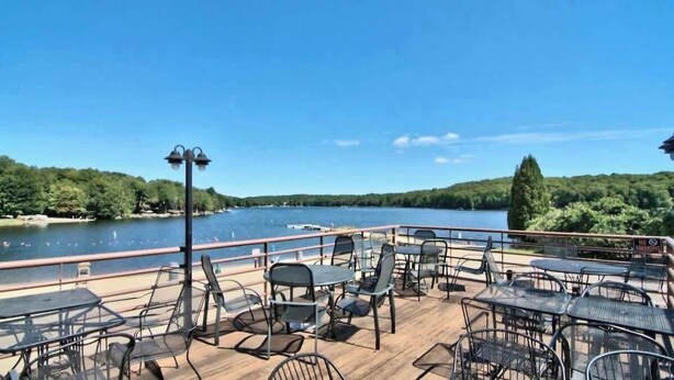 A deck with outdoor seating overlooking a lake, surrounded by greenery.