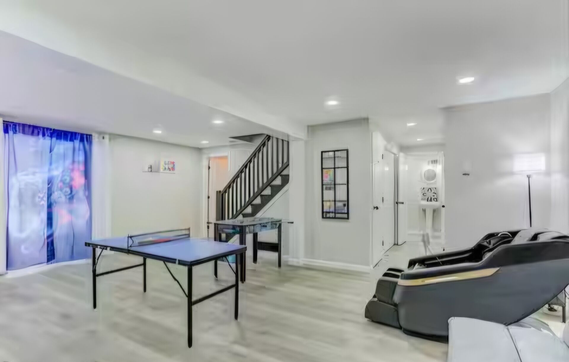 A room with a ping pong table, a massage chair, a staircase, and a door leading to another room.