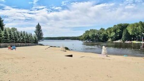 A sandy beach with a calm river, trees, and a wooden fence.