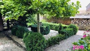 Ein Garten mit Kiesweg, ordentlich geschnittenen Hecken und einem Baum mit grünen Blättern.