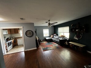Relax in this inviting living area with a large sofa and ceiling fan, surrounded by a kitchen with wooden cabinets.