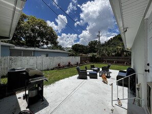 Relax in a serene outdoor space surrounded by lush greenery and trees, featuring a patio with a table, chairs, and grill.