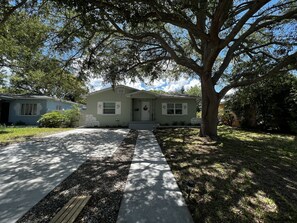 Charming single-story home with a front porch, two windows, and a large tree providing shade.