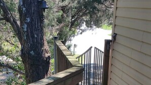 Une terrasse en bois avec une rambarde, un grand arbre et une maison en arrière-plan.