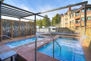 En pool på taket med en pergola, ett litet bubbelbad och utsikt över en hög byggnad.