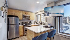 Una cocina moderna con electrodomésticos de acero inoxidable, armarios de madera, una isla grande con taburetes y vistas a montañas a través de la ventana.