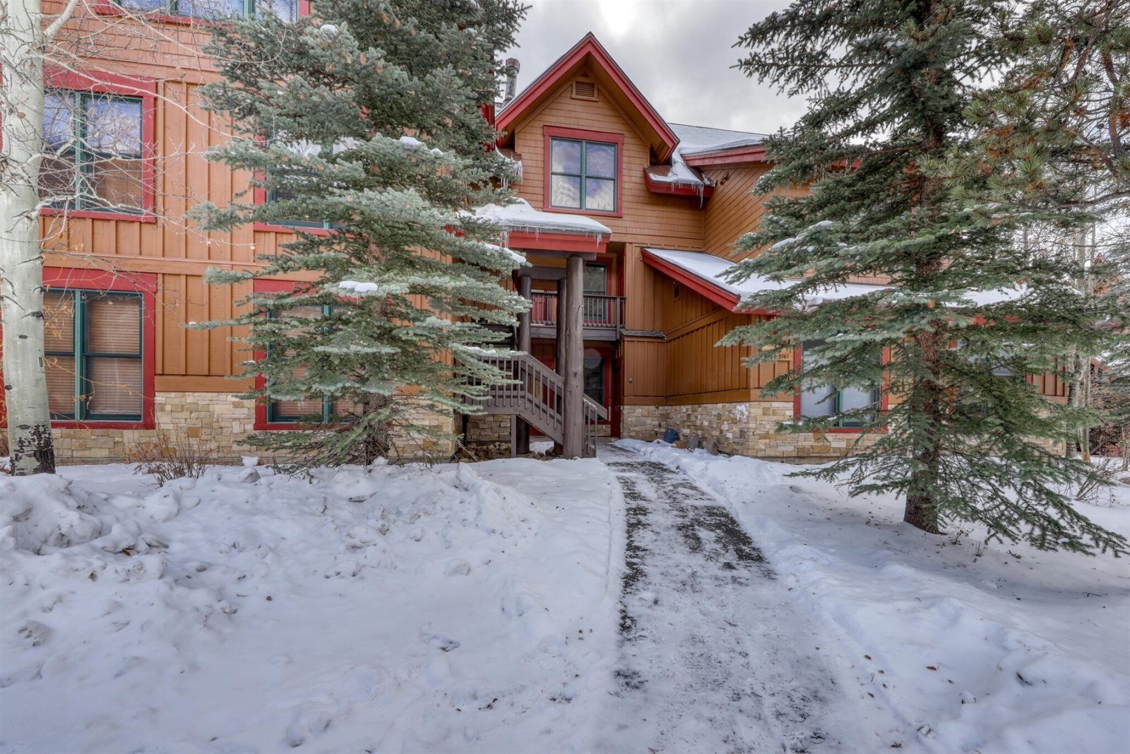 A wooden house with a stone foundation, a wooden staircase, and snow-covered ground.