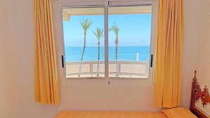 A room with a bed, a window with curtains, and a view of the sea and palm trees. - Las Vegas 3000 (Peniscola)