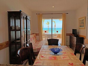 A dining area with a view of the beach, a wooden cabinet, and a table with a decorative bowl.
