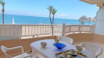 Un balcón con una mesa dispuesta para dos personas, con vista a una playa y al mar.