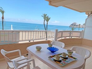 A balcony with a table set for two, overlooking a beach and the sea.