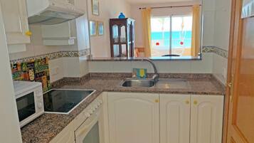 Cocina compacta con armarios blancos, encimera de granito, horno empotrado y ventana con vista a la playa.