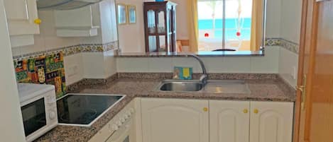 A compact kitchen with white cabinets, a granite countertop, a built-in oven, and a window with a view of the beach.