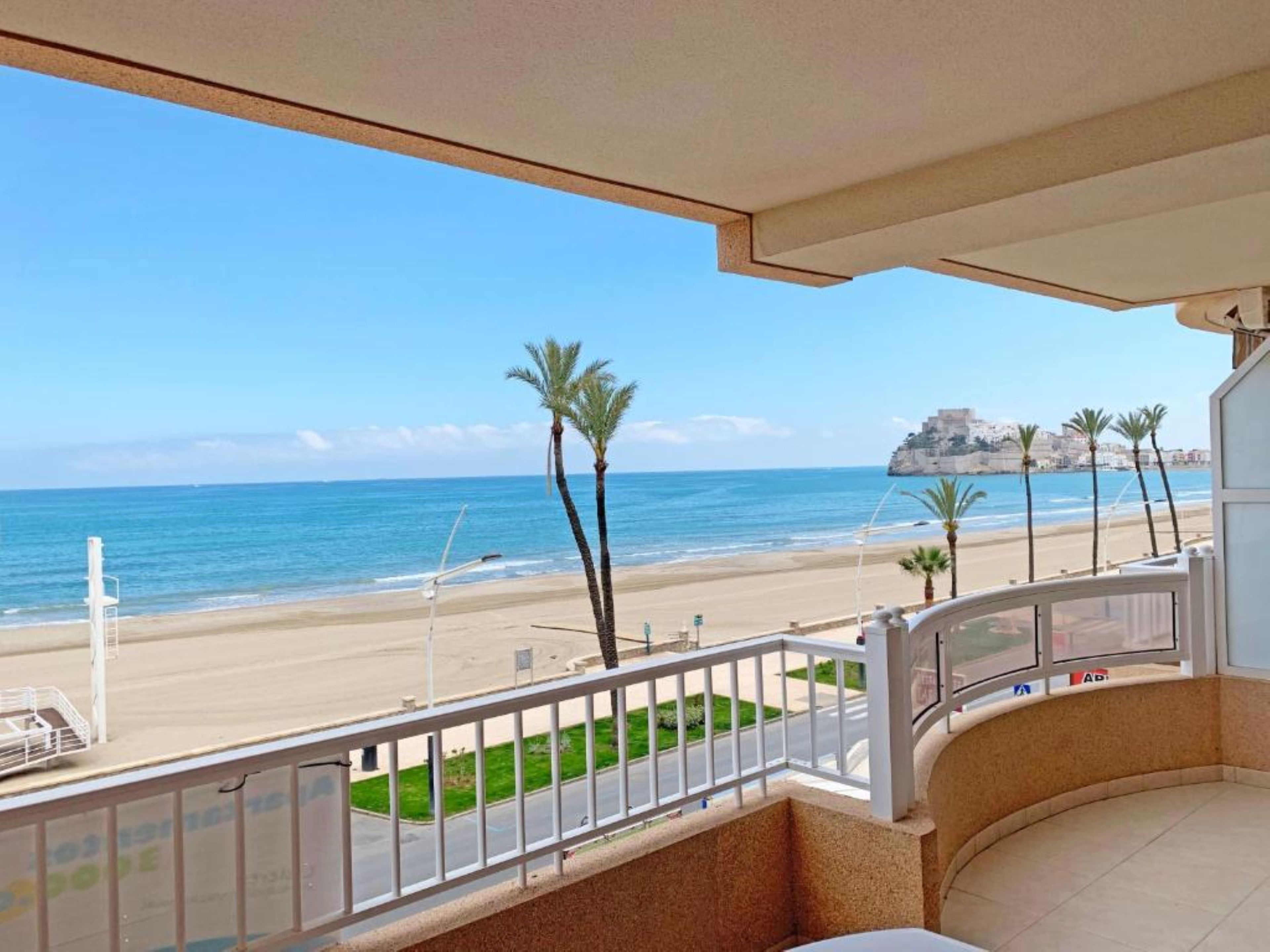 Un balcon offrant une vue sur une plage, des palmiers et un promontoire rocheux situé au loin.