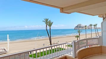 Un balcón con vista a una playa, palmeras y un promontorio rocoso distante.