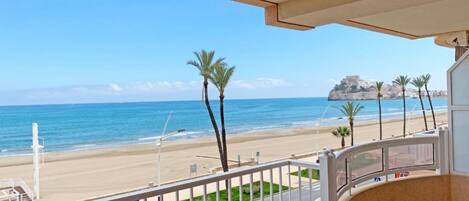 A balcony with a view of a beach, palm trees, and a distant rocky outcrop.
