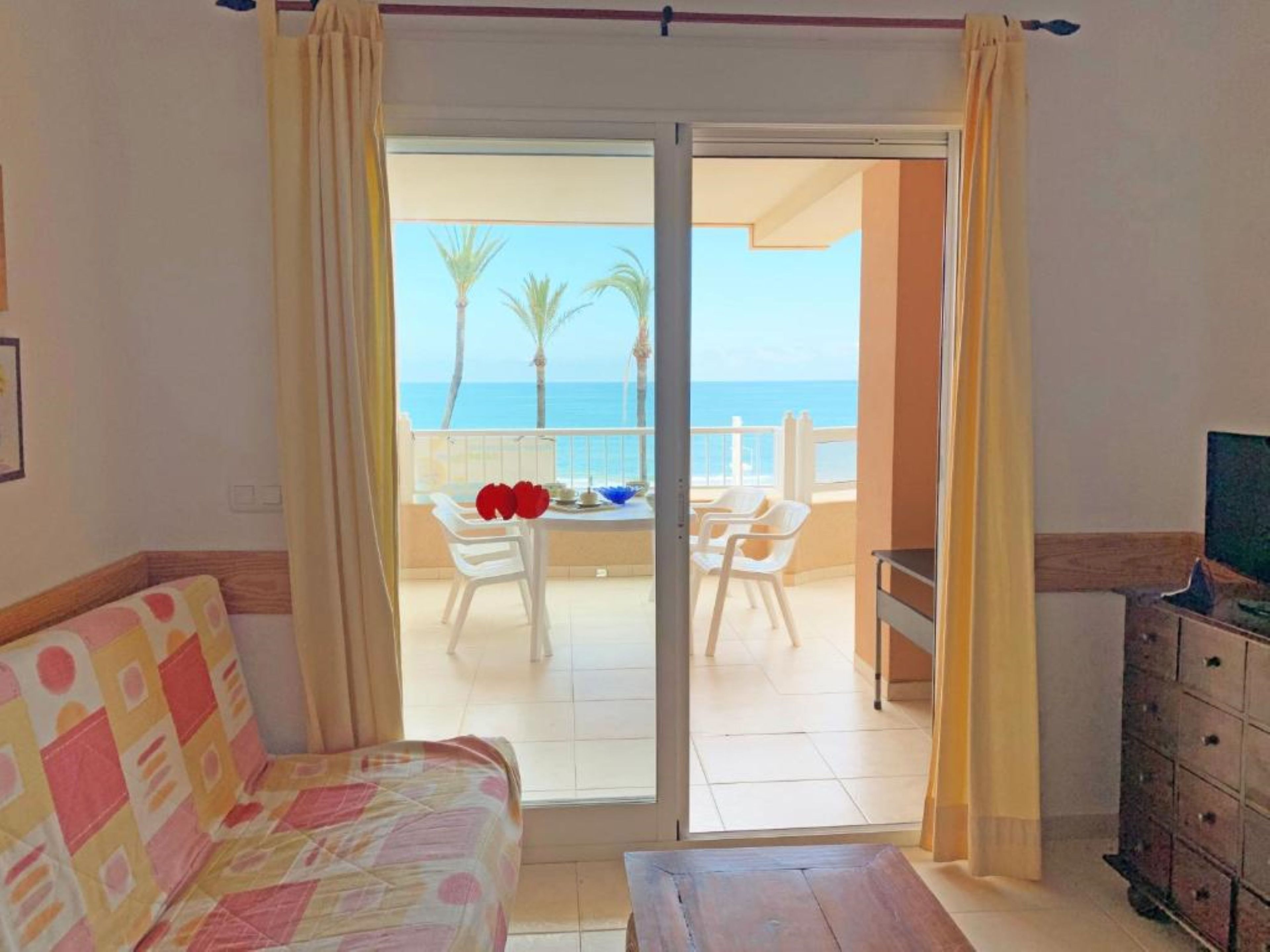 Una habitación con cama, una mesa y vista al mar por una puerta corrediza.