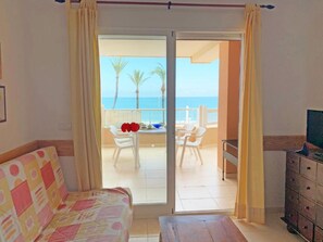 A room with a bed, a table, and a view of the sea through a sliding door.