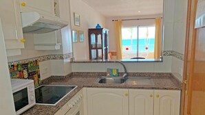 A compact kitchen with white cabinets, a granite countertop, a built-in oven, and a window with a view of the beach. - Las Vegas 3000 (Peniscola)