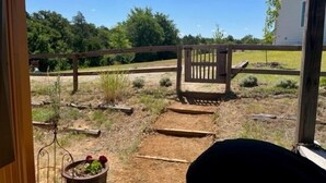 Eine Holzterrasse mit einem Metallzaun, einem Blumentopf und freiem Blick auf eine Rasenfläche mit Bäumen im Hintergrund.