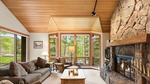 A cozy living room with a stone fireplace, large windows, and a wooden ceiling. - Luxury Ski in, Ski out 2 Bedroom Colorado Vacation Rental Steps From the Ski Slopes With Hot Tub and Pool (Snowmass Village)