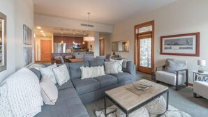 A modern living room with a grey sectional sofa, a coffee table, and a dining area in the background. - Luxury Ski in, Ski out 3 Bedroom Mountain Resort Vacation Rental in the Heart of Snowmass Base Village (Snowmass Village)