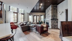 A spacious living room with a stone fireplace, large windows, and a mix of seating areas. - Premier Ski in, Ski-out 2 Bedroom Condo With Spectacular Views, Heated Outdoor Pool and Hot Tub, Short Walk to Village (Snowmass Village)