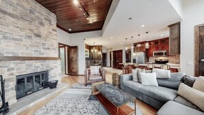 A spacious living room with a stone fireplace, a grey sofa, and a wooden ceiling. - Premier Ski in, Ski-out 2 Bedroom Condo With Spectacular Views, Heated Outdoor Pool and Hot Tub, Short Walk to Village (Snowmass Village)
