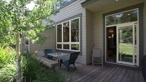 Eine überdachte Terrasse mit Tisch und Stühlen, großen Fenstern und einer Schiebetür.