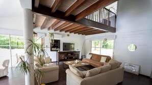 Amplia sala de estar con techo alto, vigas de madera, un conjunto de sofás, una mesa de centro y un televisor.