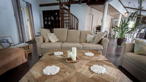 Un salón amplio con una gran mesa de centro de madera, sofá color beige y una escalera de caracol al fondo.
