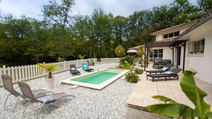 Un patio trasero con piscina, sillas de descanso y un área de patio con mobiliario exterior.