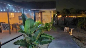 Ein gepflasterter Weg führt zu einem Haus mit Lichterketten und einer Terrassenfläche.