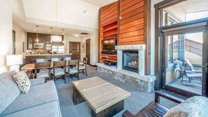 A modern living room with a fireplace, a dining area, and a kitchen in the background.