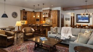 A spacious living room with a sofa, armchairs, a coffee table, and a rug. There is a kitchen area with wooden cabinets and a dining table. - Luxury 4 Bedroom Penthouse in Lionshead Village With Rooftop Pool, Just a Short Walk to Gondola (Vail)