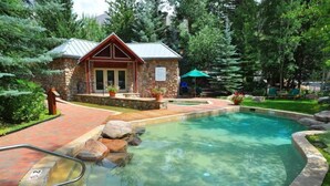 A stone building with a metal roof, a swimming pool with clear water, and surrounding greenery. - 2 Bedroom Platinum Condo Near Chairlift in Cascade Village With Pool and Hot Tub (Vail)