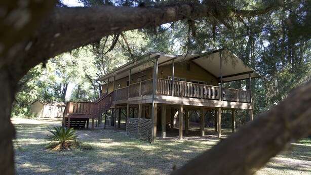 A two-story wooden cabin with a balcony, surrounded by trees.