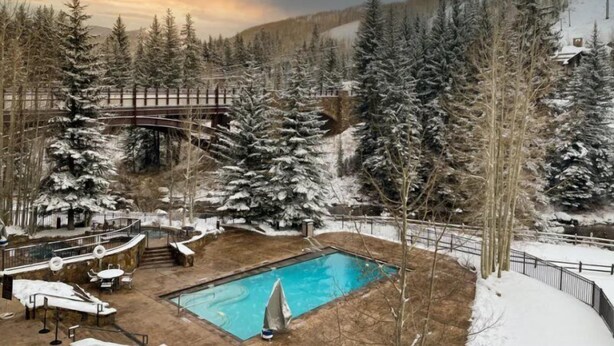 Ein verschneiter Außenbereich mit Schwimmbad, Liegestühlen und einer Holzbrücke.