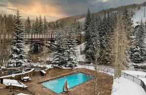 A snow-covered outdoor area with a pool, lounge chairs, and a wooden bridge.